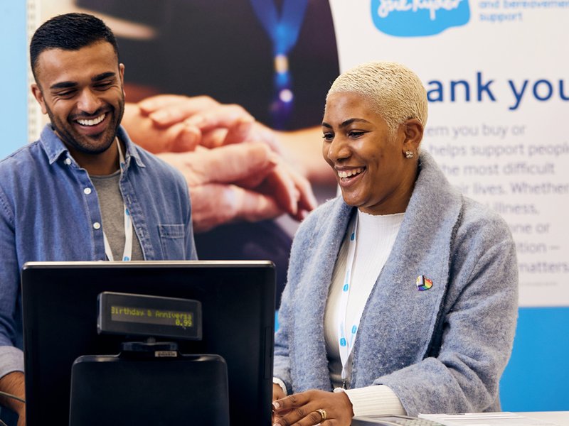 A male and female volunteer stand behind the till in a Sue Ryder charity shop