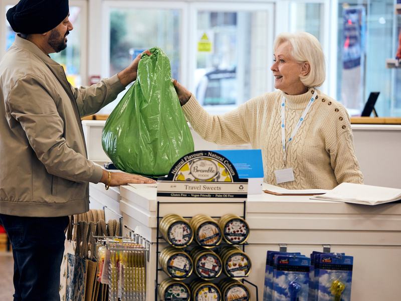 A man is handing over a bag full of donated items across the till to a staff member in a Sue Ryder shop.