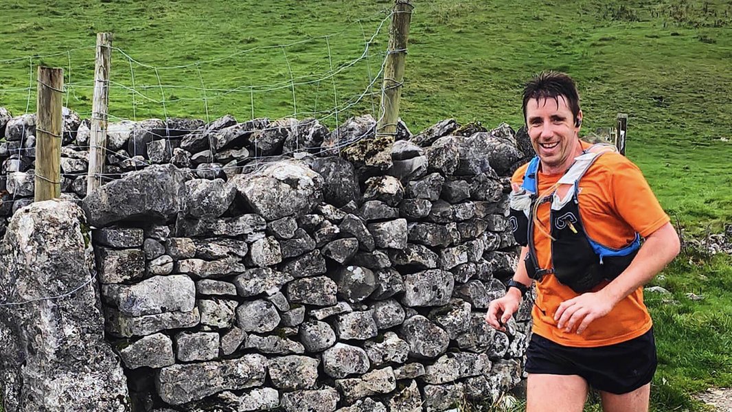 A smiling runner going past an old stone wall in the countryside