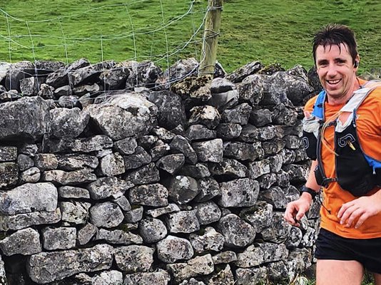 A smiling runner going past an old stone wall in the countryside