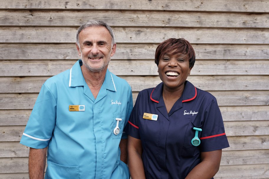 One female Sue Ryder Clinical Nurse Specialist and one male Sue Ryder Nurse smile at the camera, standing next to one another