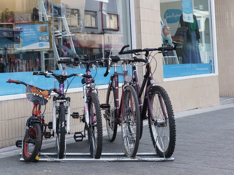 Five bikes are in a rack outside of a Sue Ryder shop. They are in size order with a small child's bike on the far left and an adult bike on the far right.