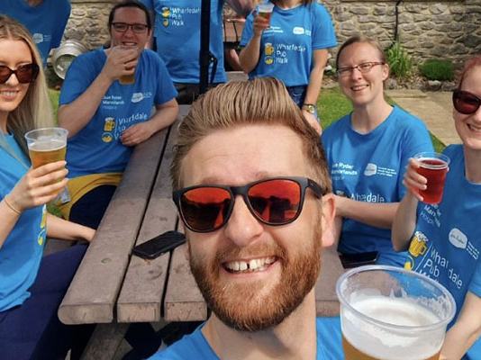A group of walkers enjoying some drinks outside at a pub bench in the sun