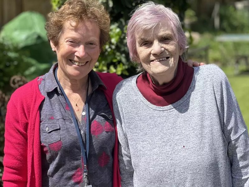 Two older women smile at the camera.