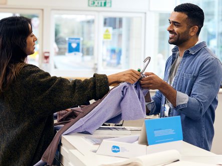 A customer buying clothes from a Sue Ryder shop assistant over the counter