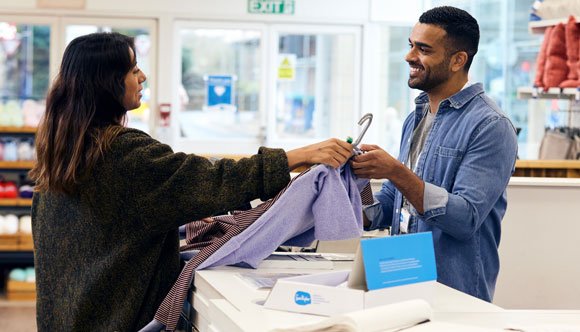 A customer buying clothes from a Sue Ryder shop assistant over the counter