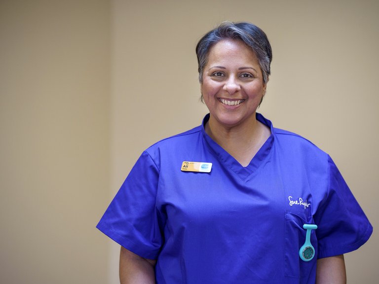 A female healthcare professional in blue scrubs is smiling at the camera.