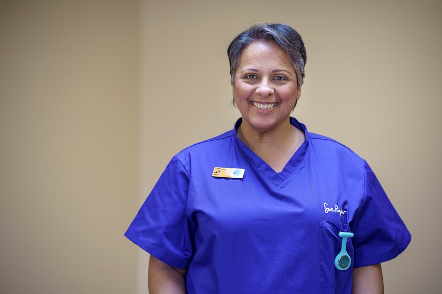 A female healthcare professional in blue scrubs is smiling at the camera.