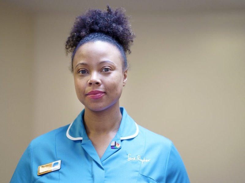 A Sue Ryder nurse, with a nametag and rainbow badge on her blue uniform