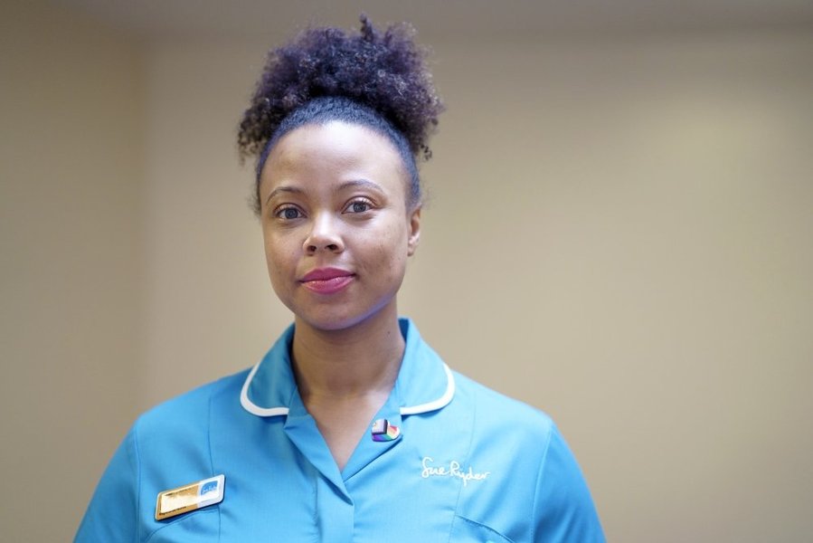 A Sue Ryder nurse, with a nametag and rainbow badge on her blue uniform