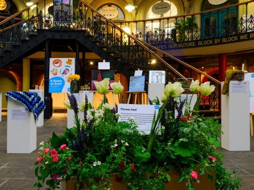 Image of Sue Ryder's Senses of Grief exhibit featuring a flower bed and other stands showing examples of the five senses of grief