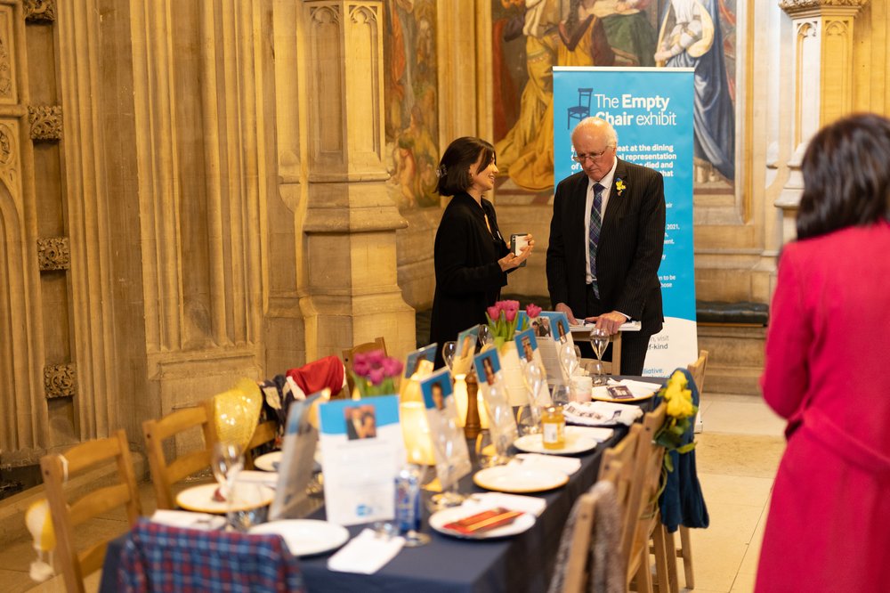 Sue Ryder's Emma Vasey and an MP near a long dining table showing personal stories in the empty spaces
