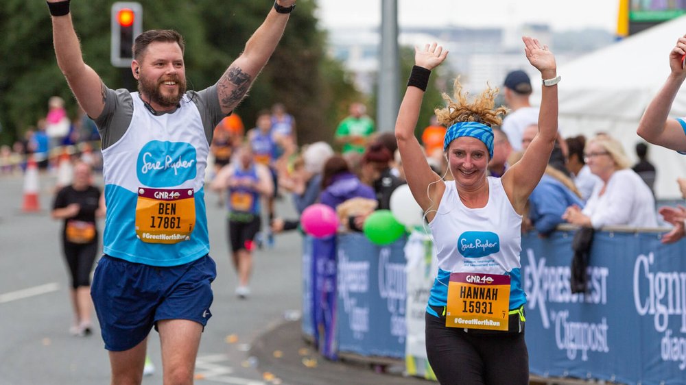 Two Sue Ryder Runners smiling at camera with arms in the air in celebration.