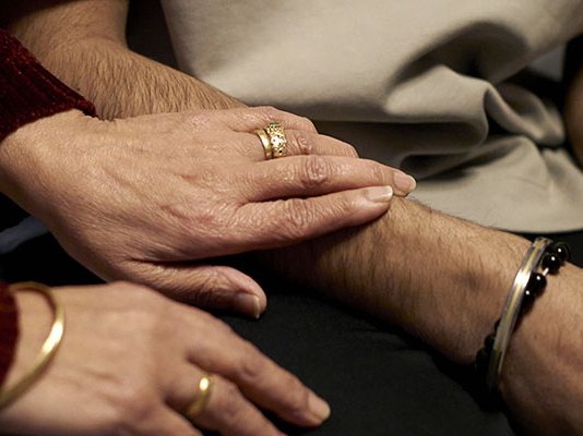 Close up of a grieving mother comforting her grieving son, putting her hand on his arm