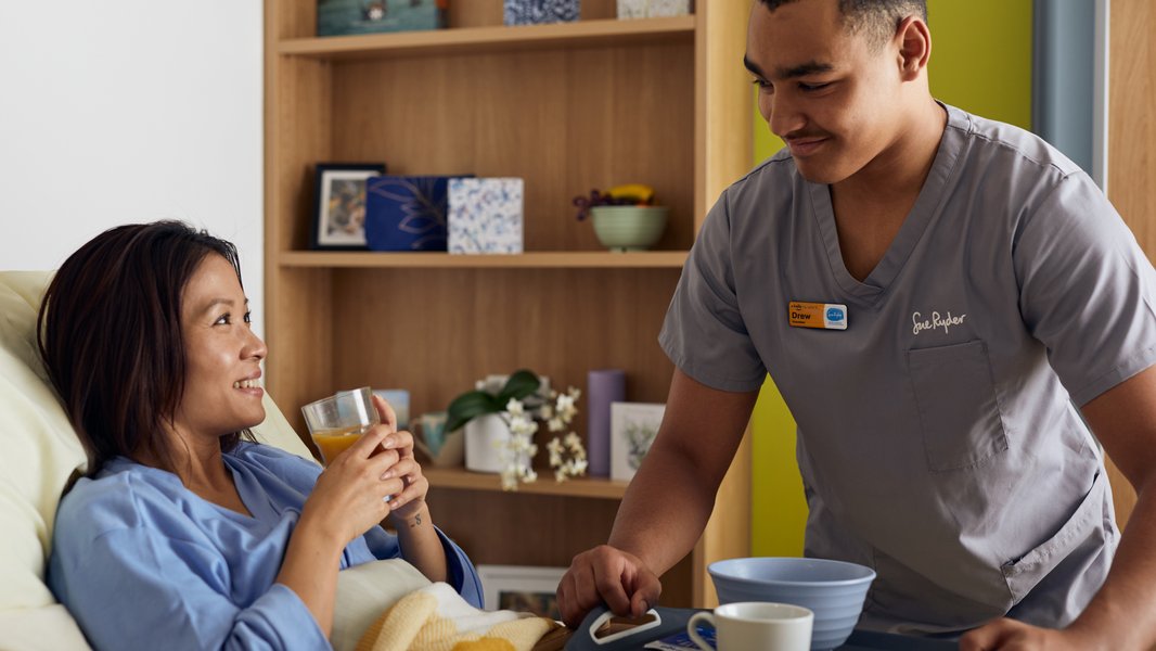A Sue Ryder hospice volunteer serving breakfast to a patient in bed