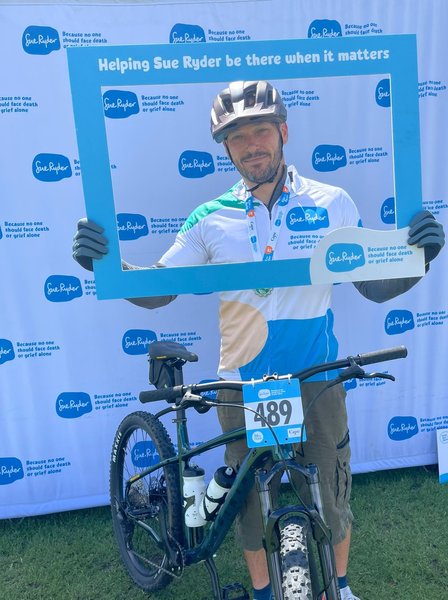 A Sue Ryder cyclist with their bike, holding a blue Sue Ryder frame around their head