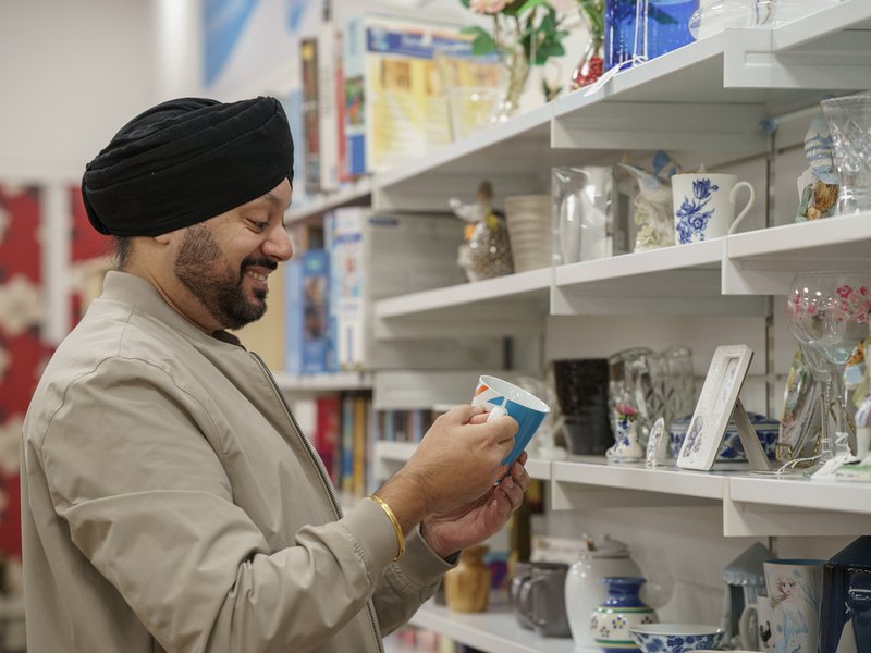 A shop customer is looking at shelves of bric a brac and holding an item