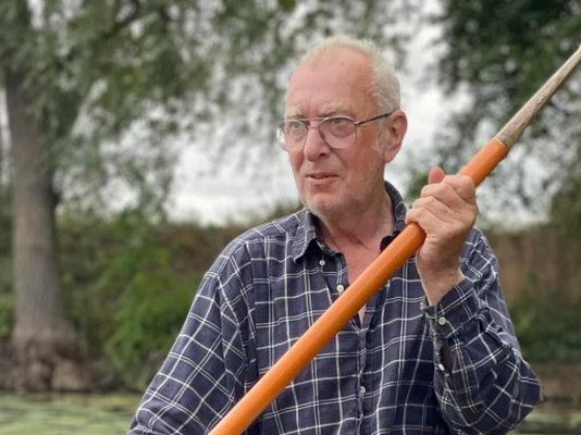 Norman Ward, sitting in a rowing boat holding an oar on a pond