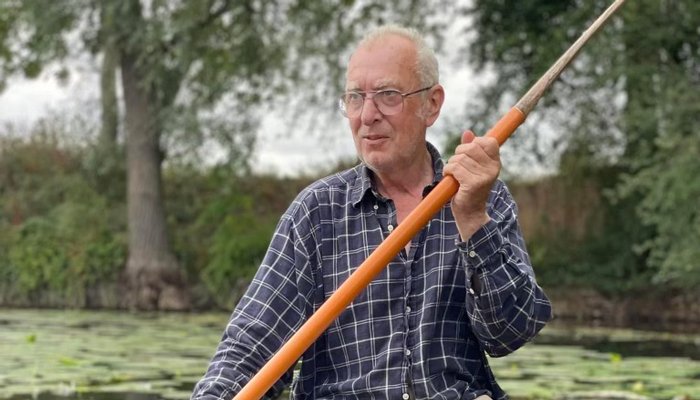 Norman Ward, sitting in a rowing boat holding an oar on a pond