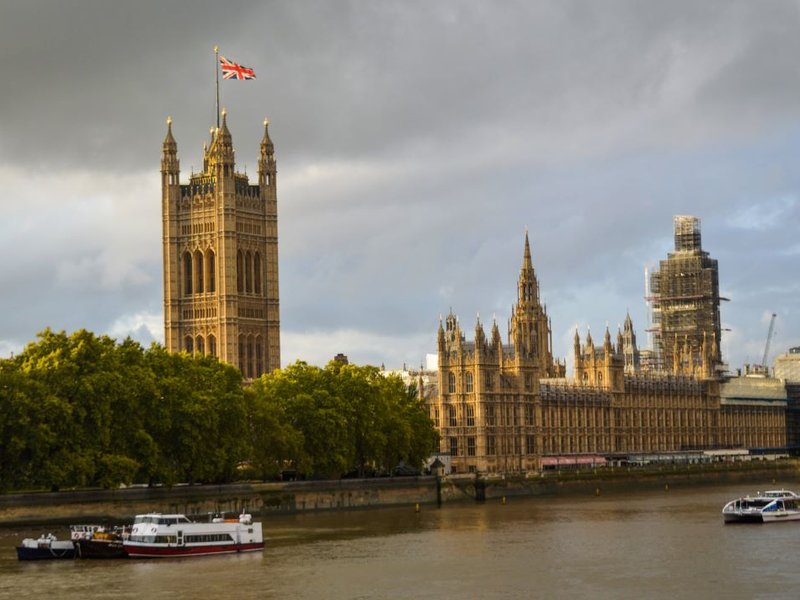 The Houses of Parliament building, next to the River Thames where boats float by