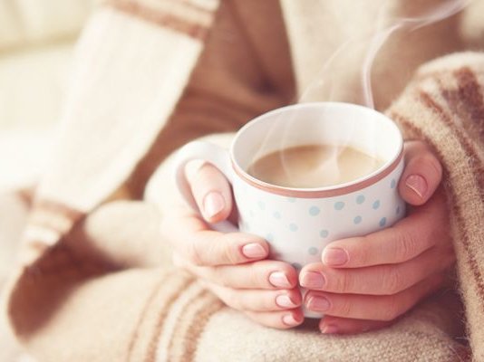 A person wrapped in a blanket, holding a hot cup of tea