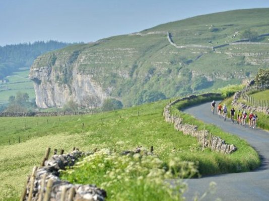 Le Petit Depart riders racing along a country lane in the distance, surrounded by the Yorkshire Dales
