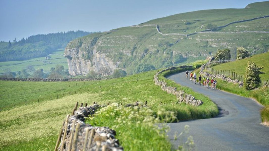 Le Petit Depart riders racing along a country lane in the distance, surrounded by the Yorkshire Dales