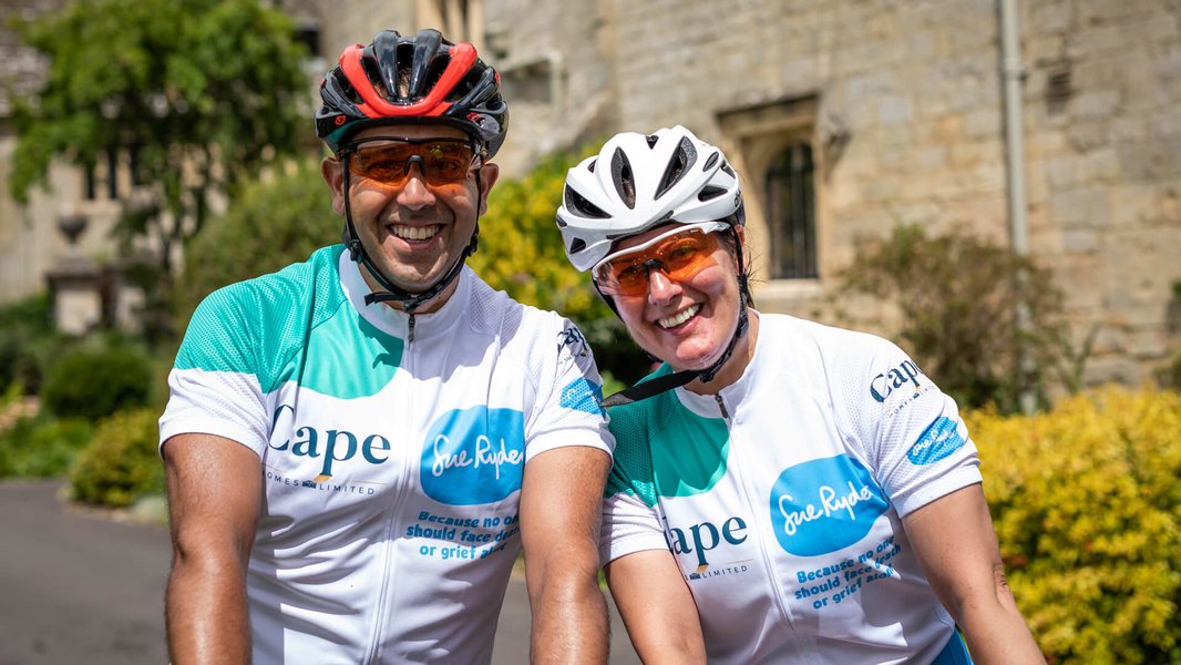 Two cyclists in their helmets and Sue Ryder cycling jerseys, smiling and hugging