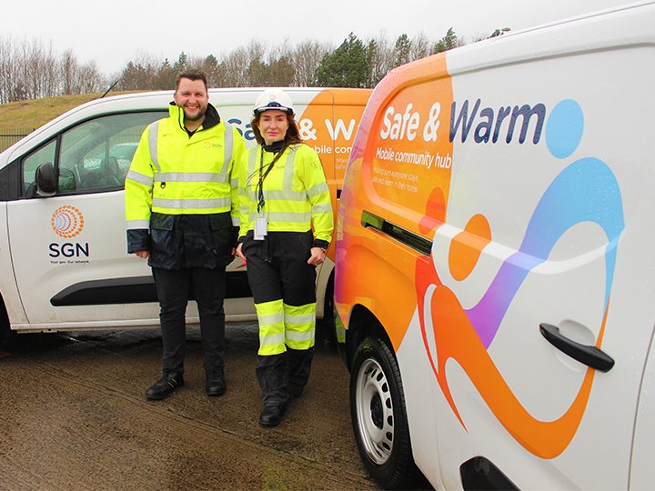 Two SGN employees dressed in high-vis jackets stand next to vans with "safe and warm" written on them