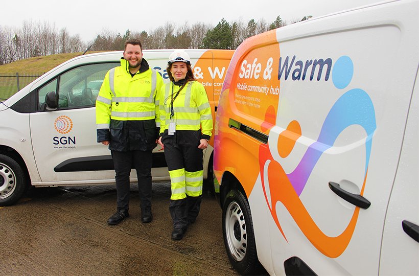 Two SGN employees dressed in high-vis jackets stand next to vans with "safe and warm" written on them