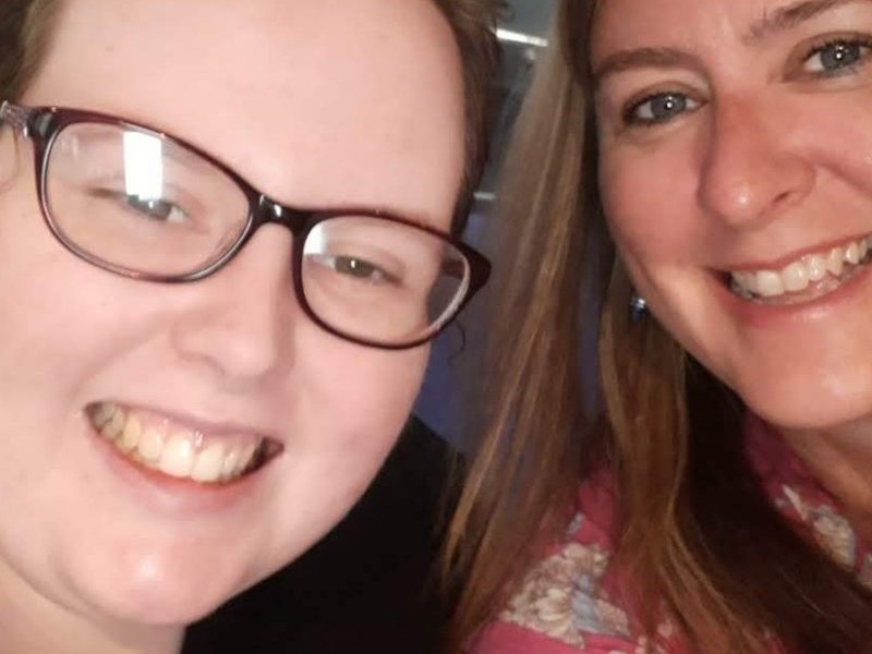 A selfie of Sarah (right) and Laura (left) - both are smiling at the camera. Laura is wearing a black top and glasses and Sarah is wearing a pink top.