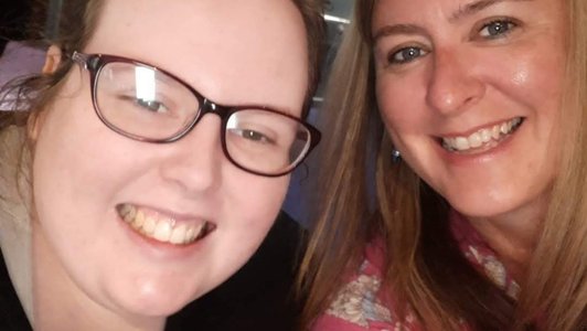 A selfie of Sarah (right) and Laura (left) - both are smiling at the camera. Laura is wearing a black top and glasses and Sarah is wearing a pink top.