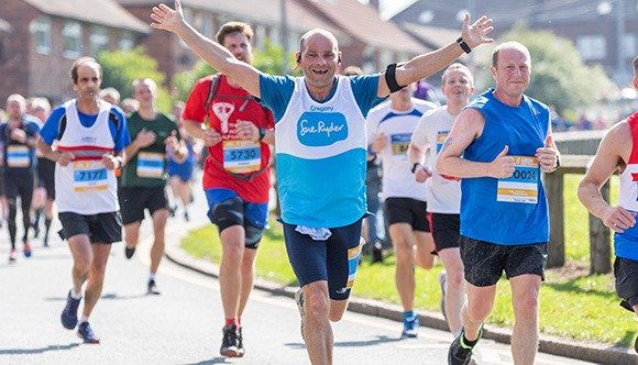 A Sue Ryder runner during a race, with his hands in the air