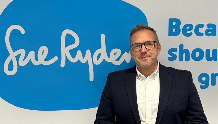 Sue Ryder CEO, James Sanderson, in front of a Sue Ryder sign