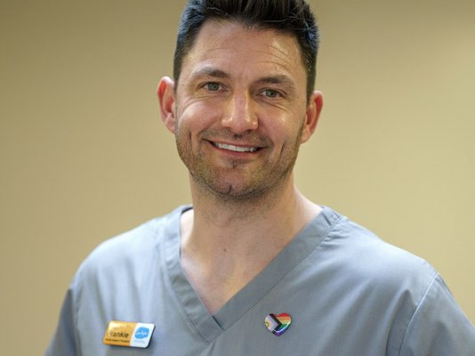 A smiling male Sue Ryder healthcare staff member in a green uniform