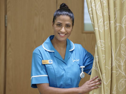 A smiling Sue Ryder Nurse opening a curtain in a hospice room