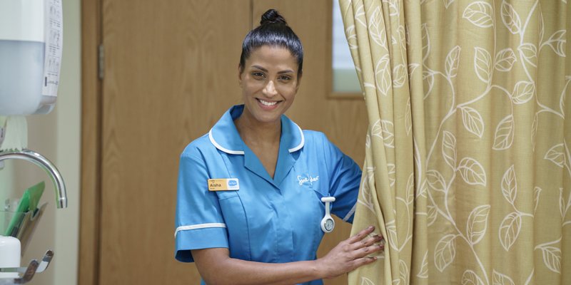 A smiling Sue Ryder Nurse opening a curtain in a hospice room