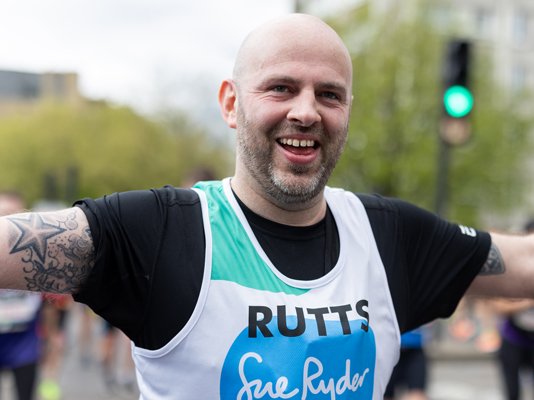 A Sue Ryder runner on the race route, celebrating with their arms in the air