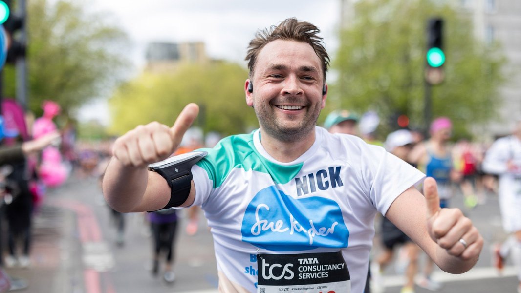 A smiling Sue Ryder runner giving the thumbs as he races down the street
