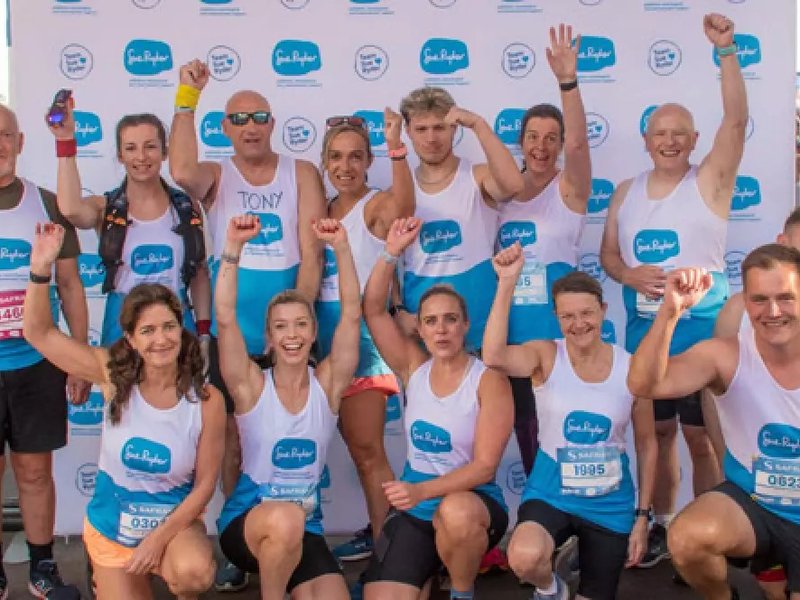 A group of people wearing Sue Ryder running shirts cheer for the camera.