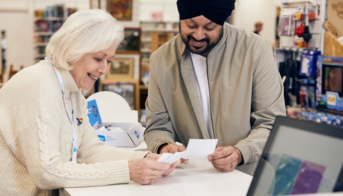 A Sue Ryder shop volunteer serving a customer at the till
