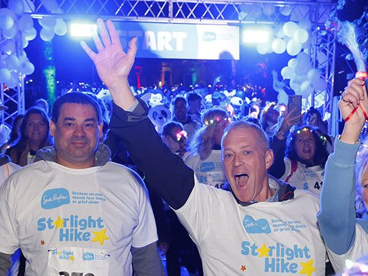 Four Starlight Hikers celebrating at the starting line, surrounded by other walkers and neon lights