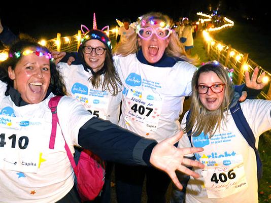 A group of Starlight Hike walkers in bright neon clothing, with the light trail glowing behind them