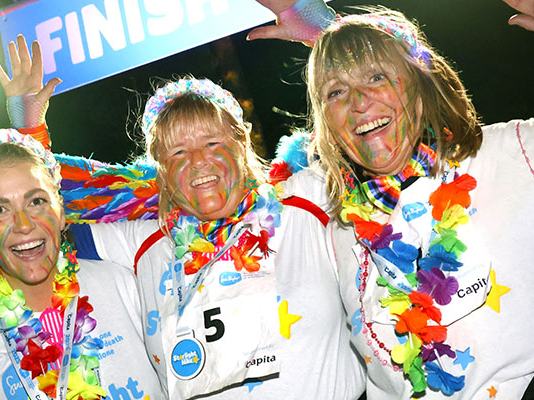 Three Starlight Hike walkers in rainbow clothes and face paint, celebrating at the finish line with their medals