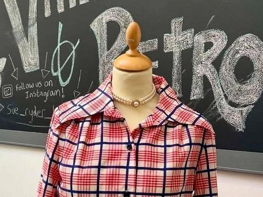 A vintage dress on a stand, in front of a blackboard saying 'Sue Ryder Bedford - Vintage and Retro'