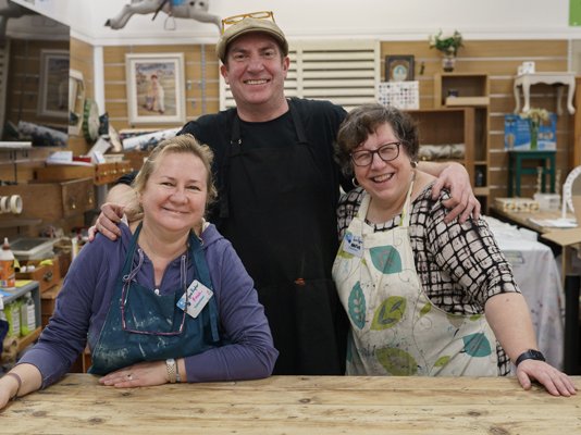 Three Sue Ryder volunteers together in the upcycling workshop, surrounded by upcycled items