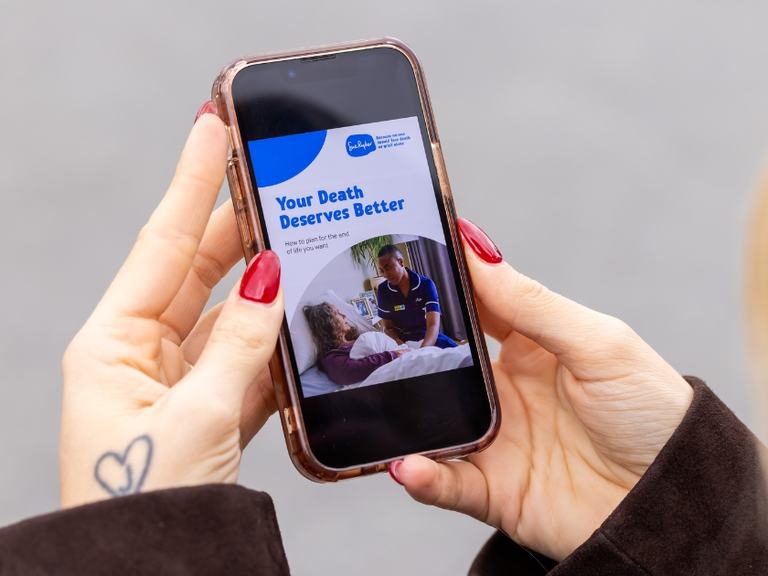 Person holding a smartphone displaying a Sue Ryder guide titled ‘Your Death Deserves Better’ about end-of-life care.