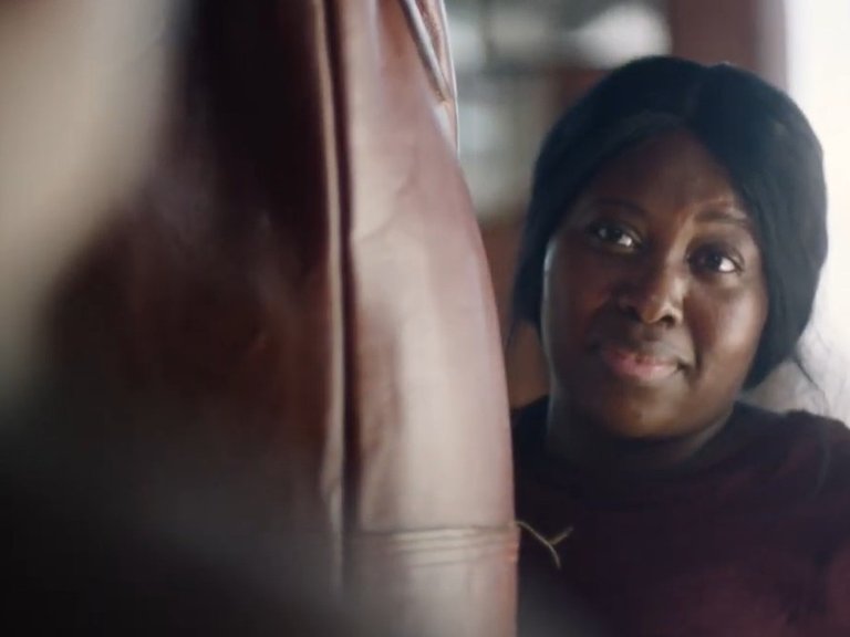 A woman stands behind a punchbag in the gym, smiling at her friend