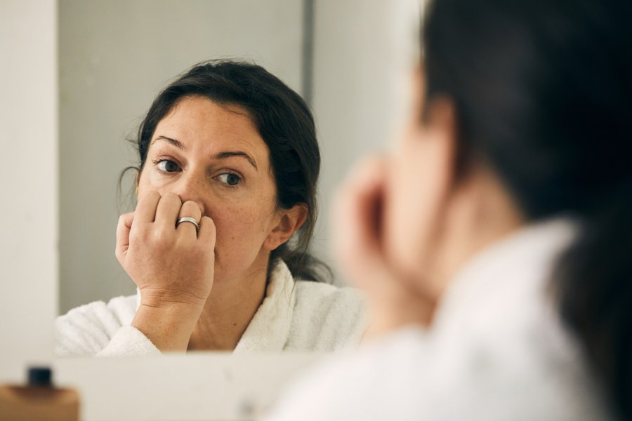 A woman looks into a mirror with her hand up to her mouth.