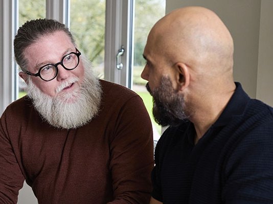 Two men sitting together in their kitchen, discussing funeral plans